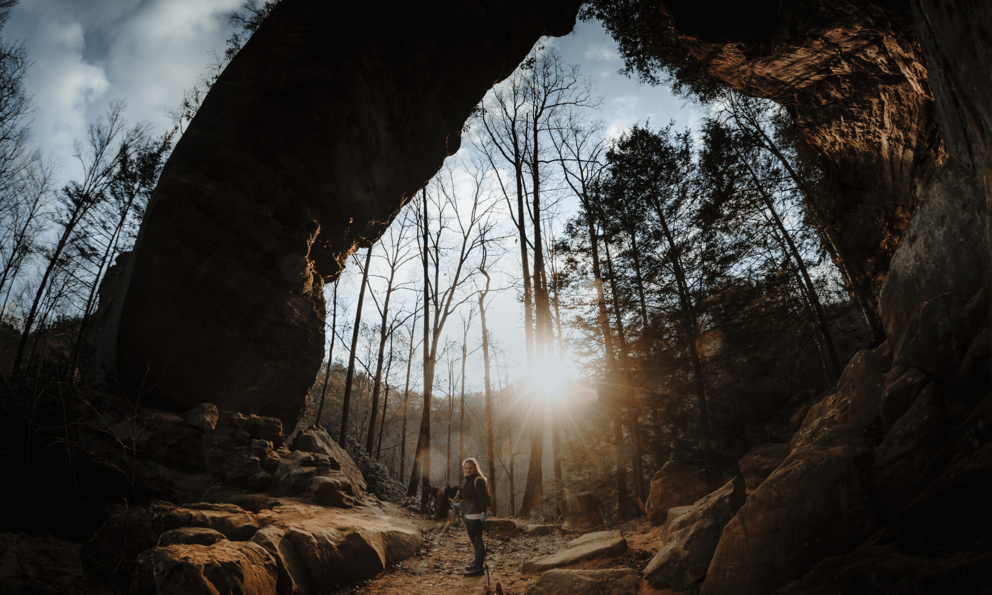 Woman hiker and her dog dwarfed by the massive Gray's Arch in Red River Gorge, Kentucky.
