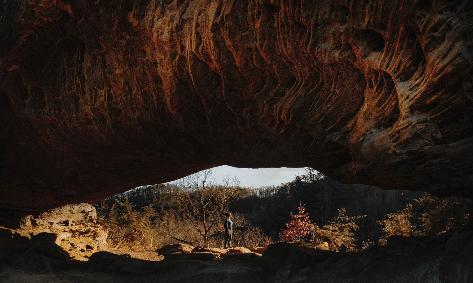 Woman standing under huge natural rock arch in Red River Gorge, Kentucky. Star Gap Arch.