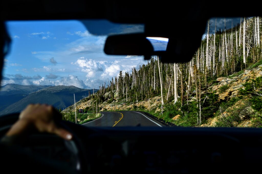 View from inside the cab of a truck of a road, mountains and aspens.