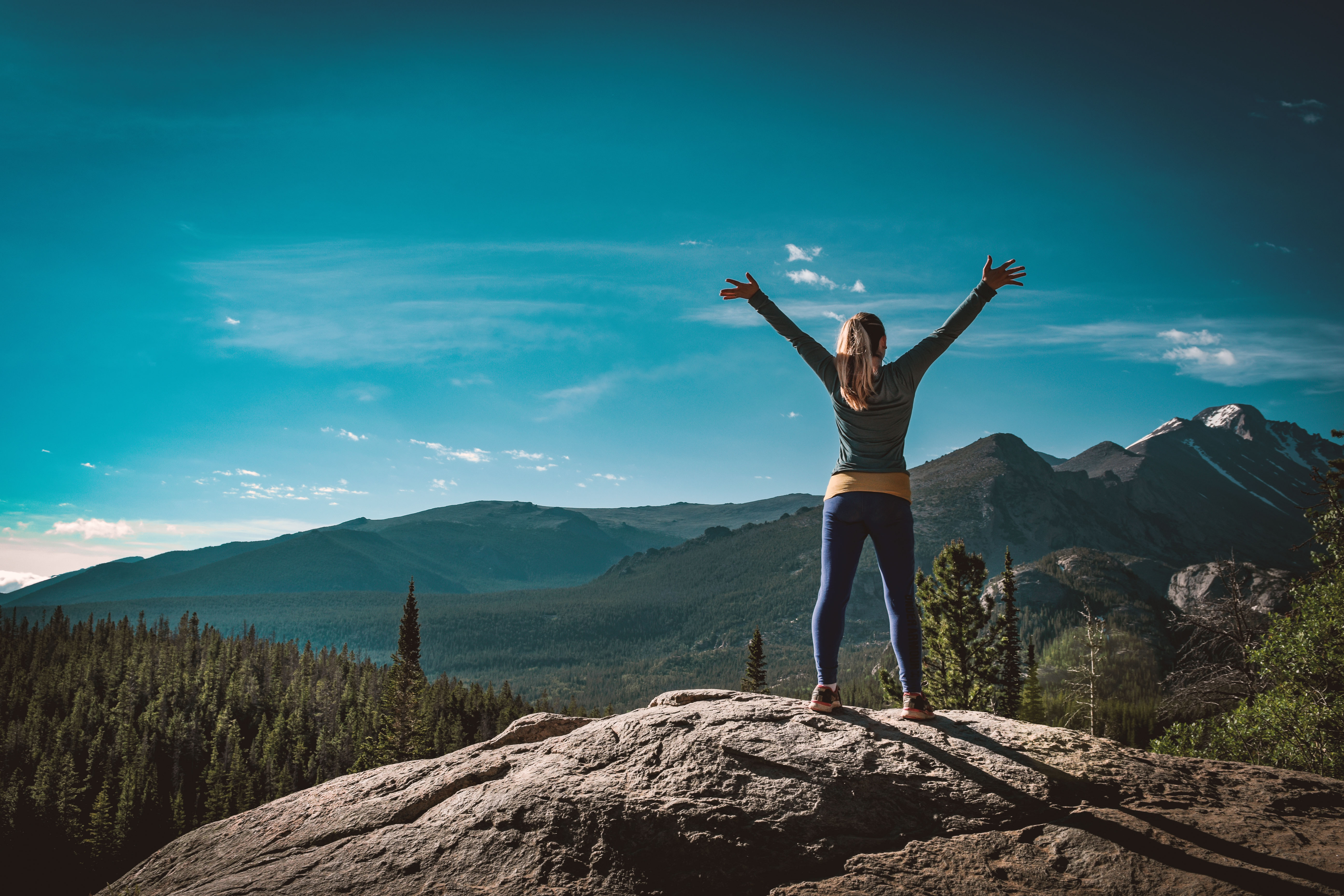 Kat stands atop a rocky bluff overlooking mountains