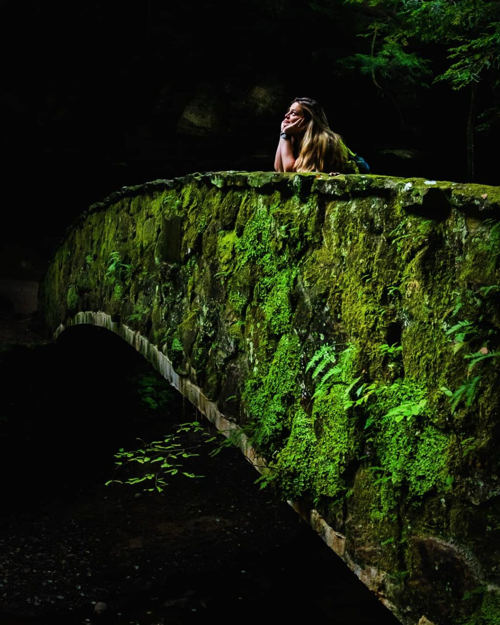 Woman looking longingly with her head in her hands on a stone bridge.