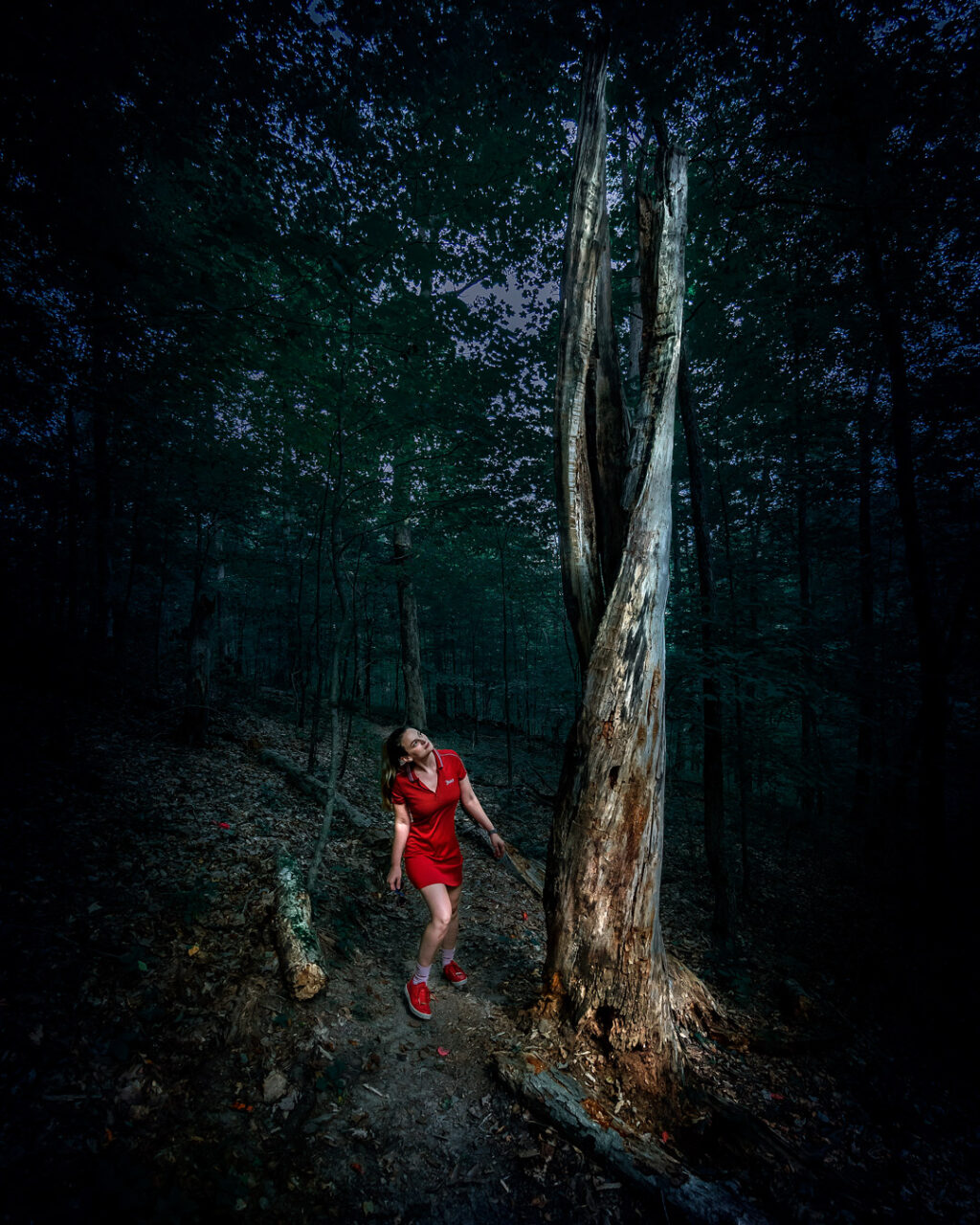 Woman hiker in red dress looking at a dead tree in the forest.