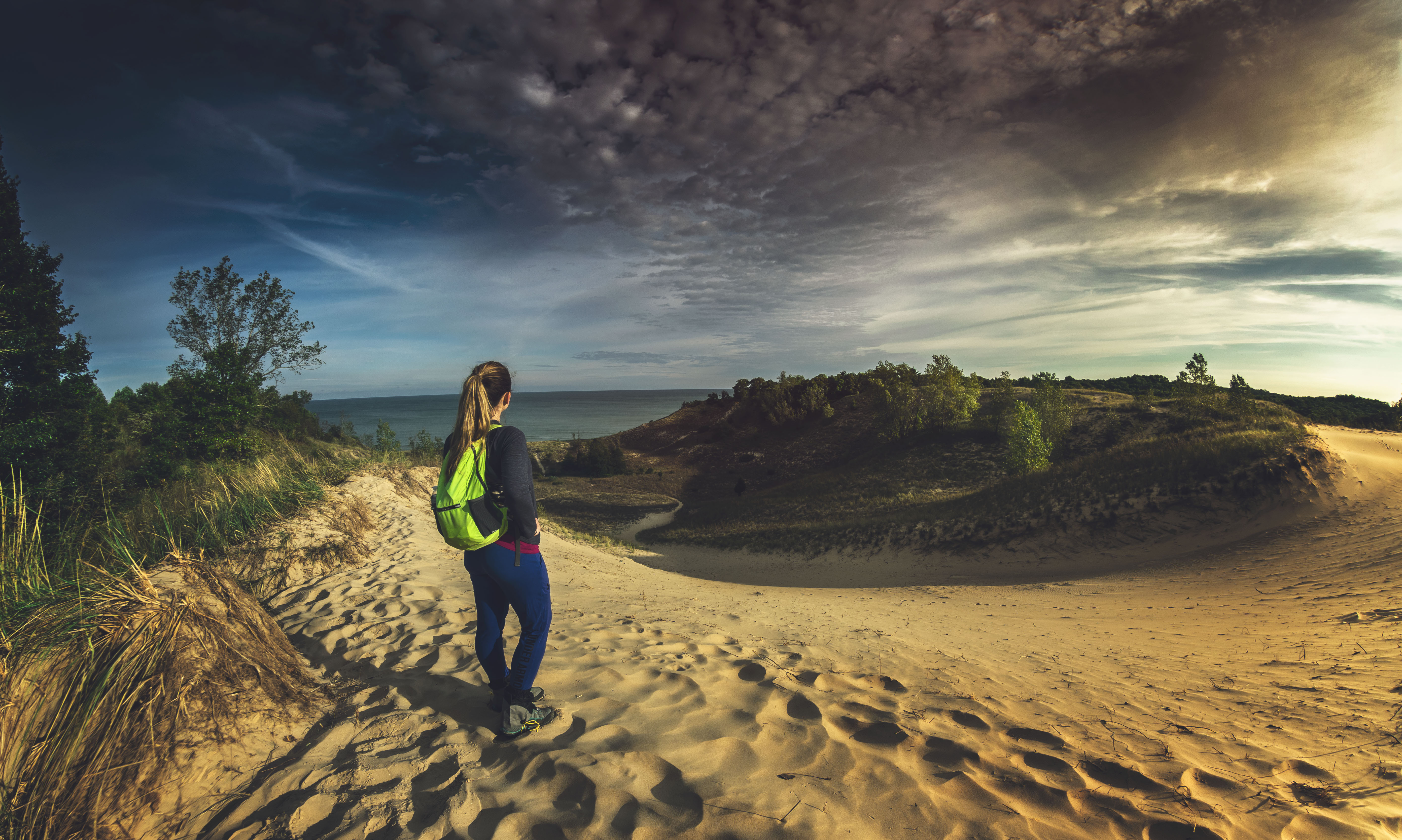 Woman hiker standing atop sand dune overlooking Lake Michigan at Indiana Dunes State Park.