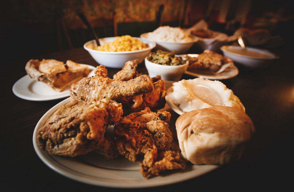 Plate of fried chicken with mashed potatoes, gravy and a biscuit, surrounded by side orders.