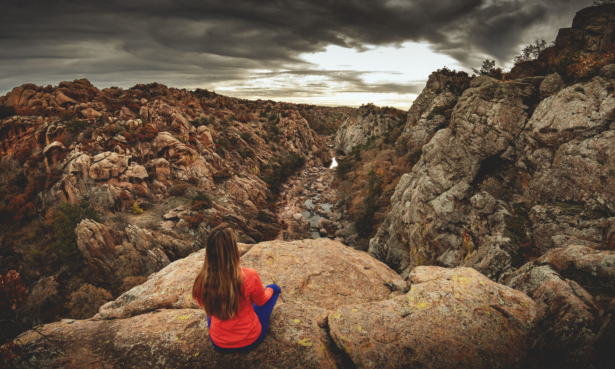 Woman hiker sitting on edge of cliff overlooking The Narrows canyon at Wichita Mountains Wildlife Refuge in Oklahoma.