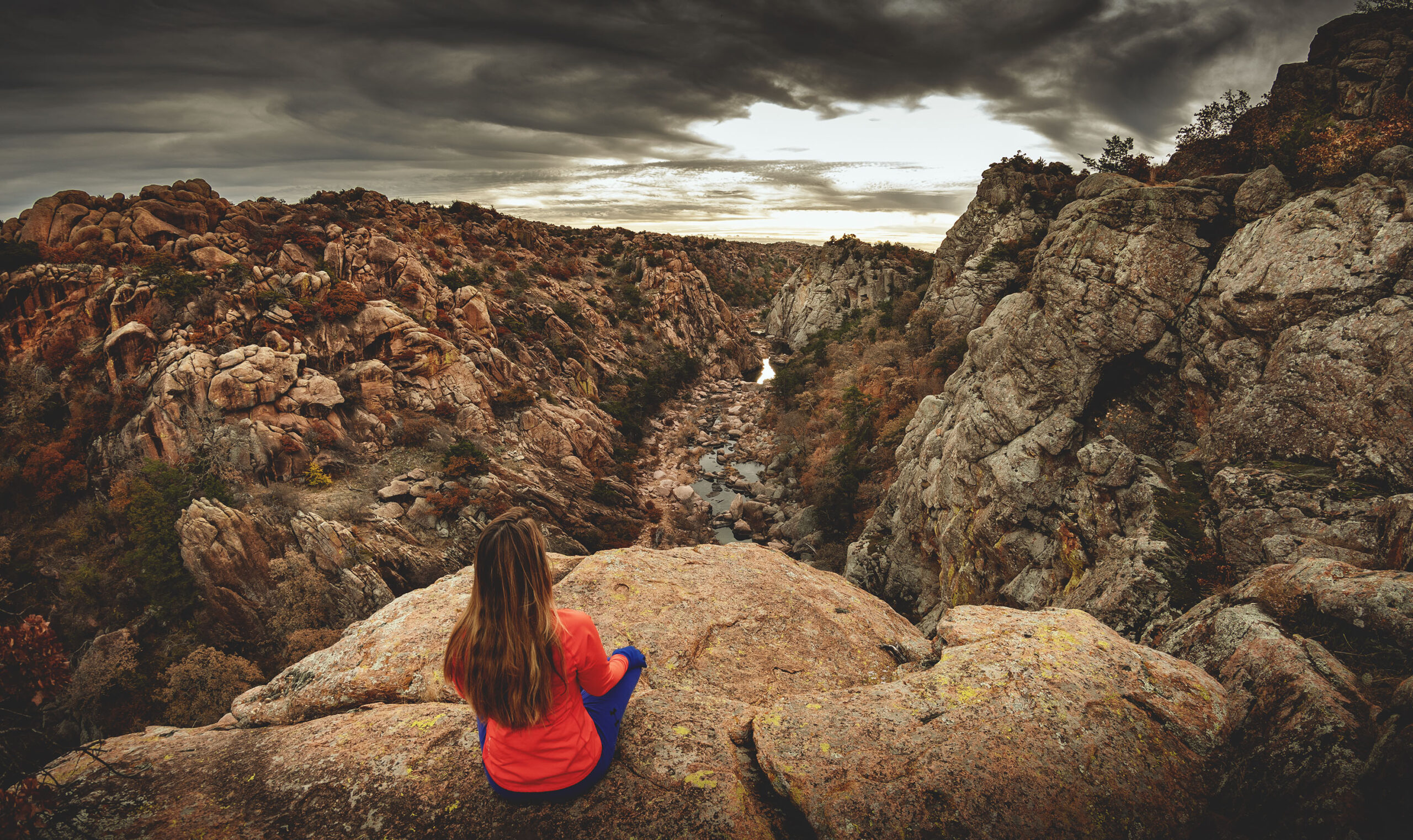 Woman hiker sitting on edge of cliff overlooking The Narrows canyon at Wichita Mountains Wildlife Refuge in Oklahoma.