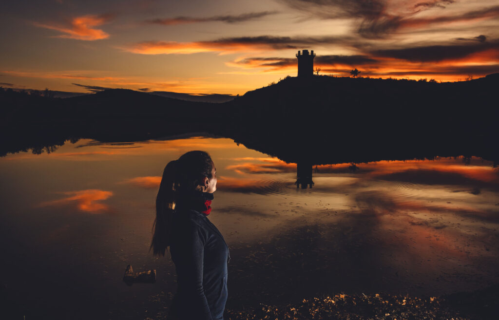 Woman hiker watching sunset over lake with Jed Johnson Tower reflected in water, Wichita Mountains Wildlife Refuge, Oklahoma.