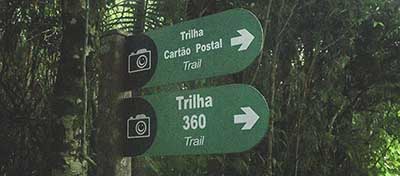 Green trailhead signs point to Trilha Cartao Postal (the Postcard Trail) and Trilha 360.