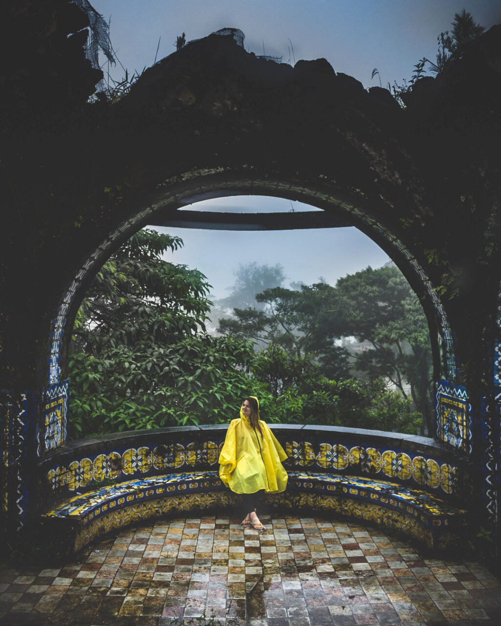 Woman in yellow poncho sitting among the ruins of Quiosque das Lendas in Teresopolis, Brazil.
