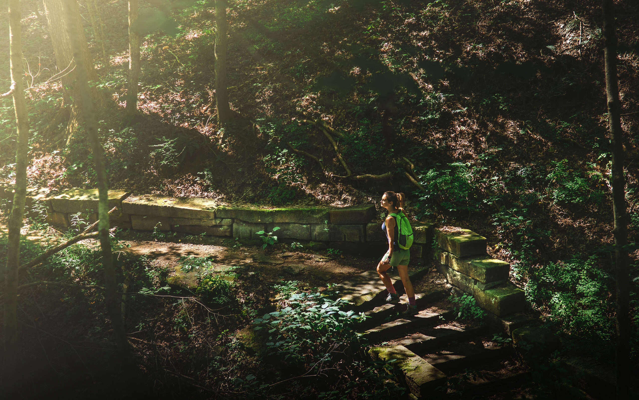 Woman hiking up stone stairway in the sun-dappled forest on Trail 2, Brown County State Park, Indiana.