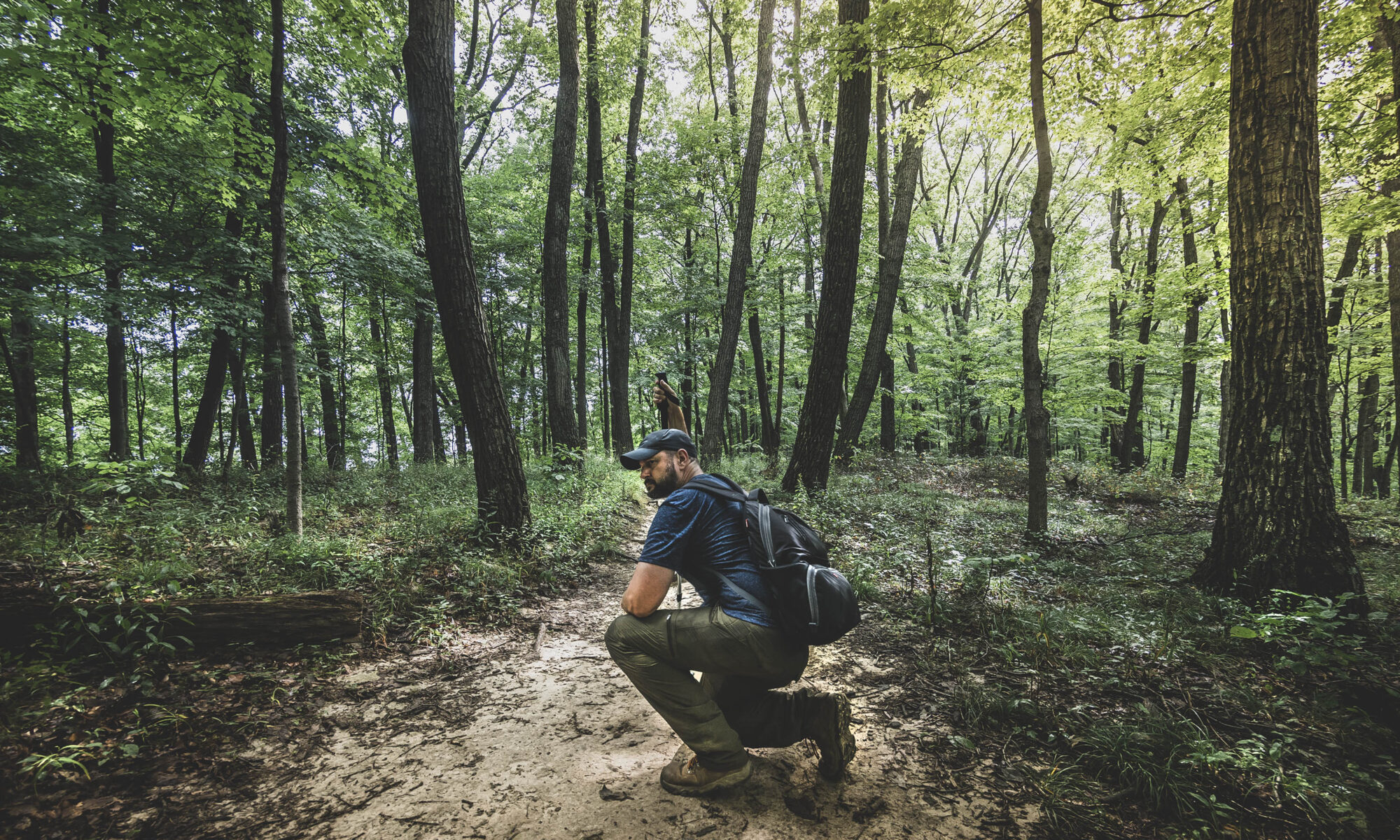 Male hiker crouching on a hiking trail in the forest at Brown County State Park, Indiana.