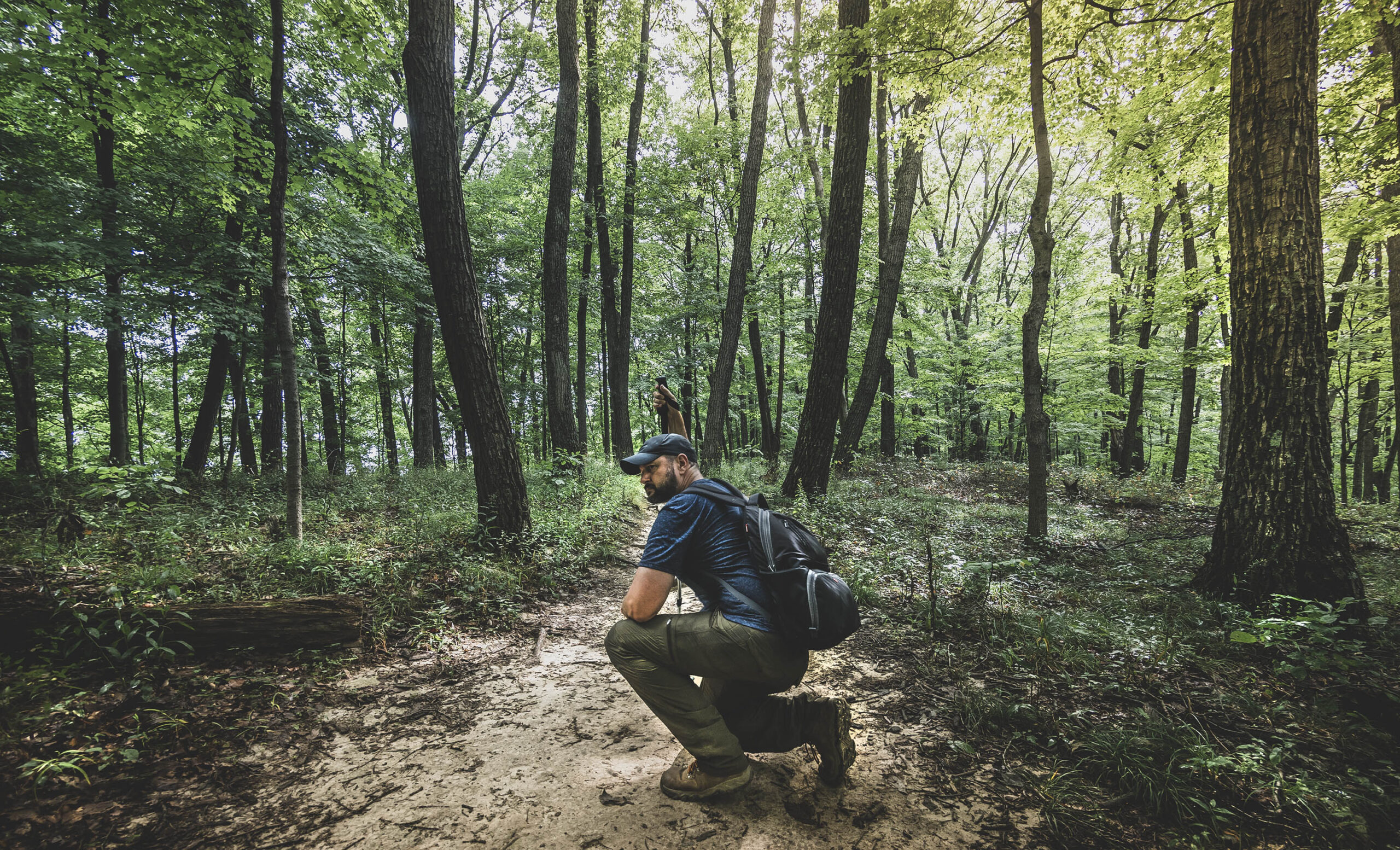 Male hiker crouching on a hiking trail in the forest at Brown County State Park, Indiana.