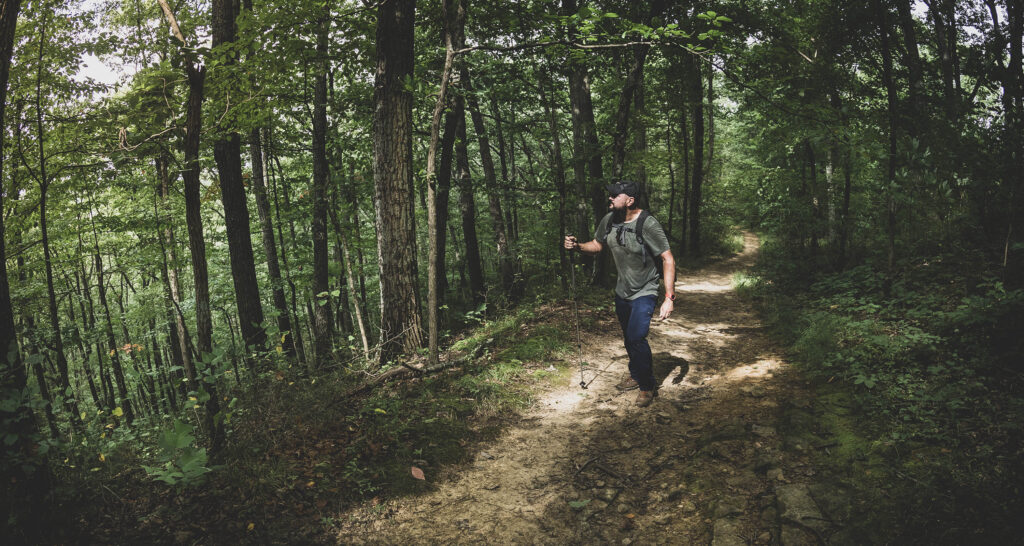 Man hiking on a dirt trail in dense green forest on Trail 11 at Brown County State Park, Indiana.