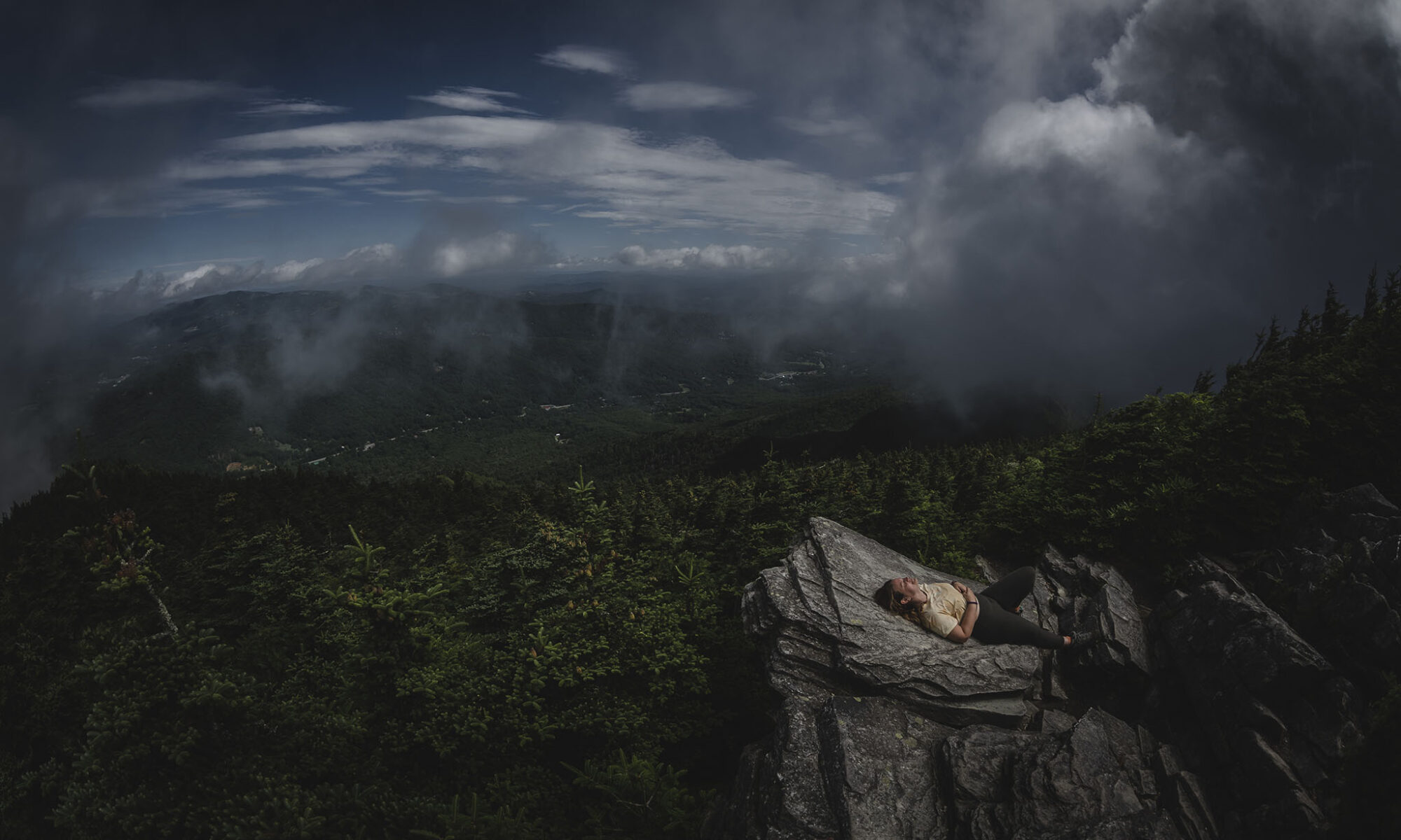 Woman hiker resting on a rocky outcrop overlooking Blue Ridge Mountains at Watauga View, Grandfather Mountain.
